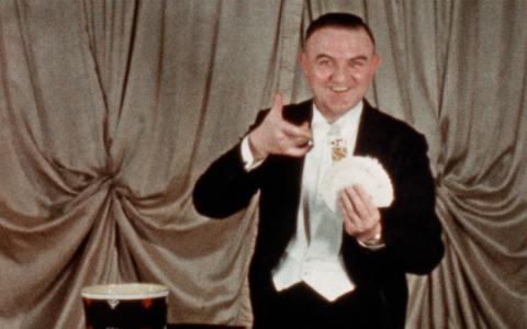Magician Lewis Ganson in evening dress holding a fan of cards
